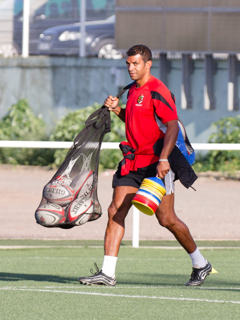 Éducateur portant des ballons de rugby sur un terrain à Toulouse